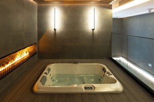 A modern bathroom with a freestanding bathtub, a wooden floor, and a wall-mounted light fixture.