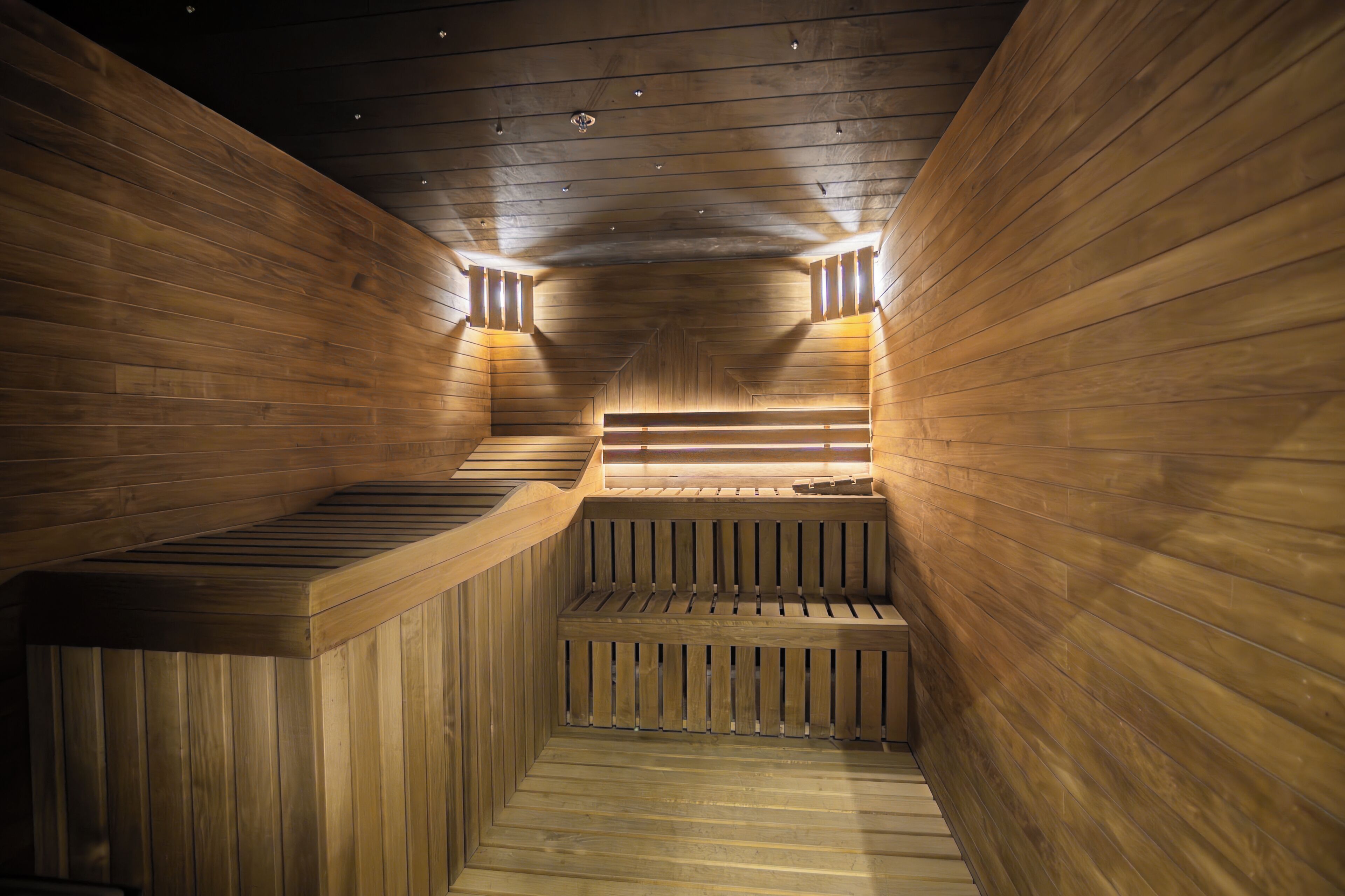 Eine Sauna mit Holzwänden und -bänken, mit einer Mittelbank und einer leicht abfallenden Fläche, die in eine untere Ebene führt.