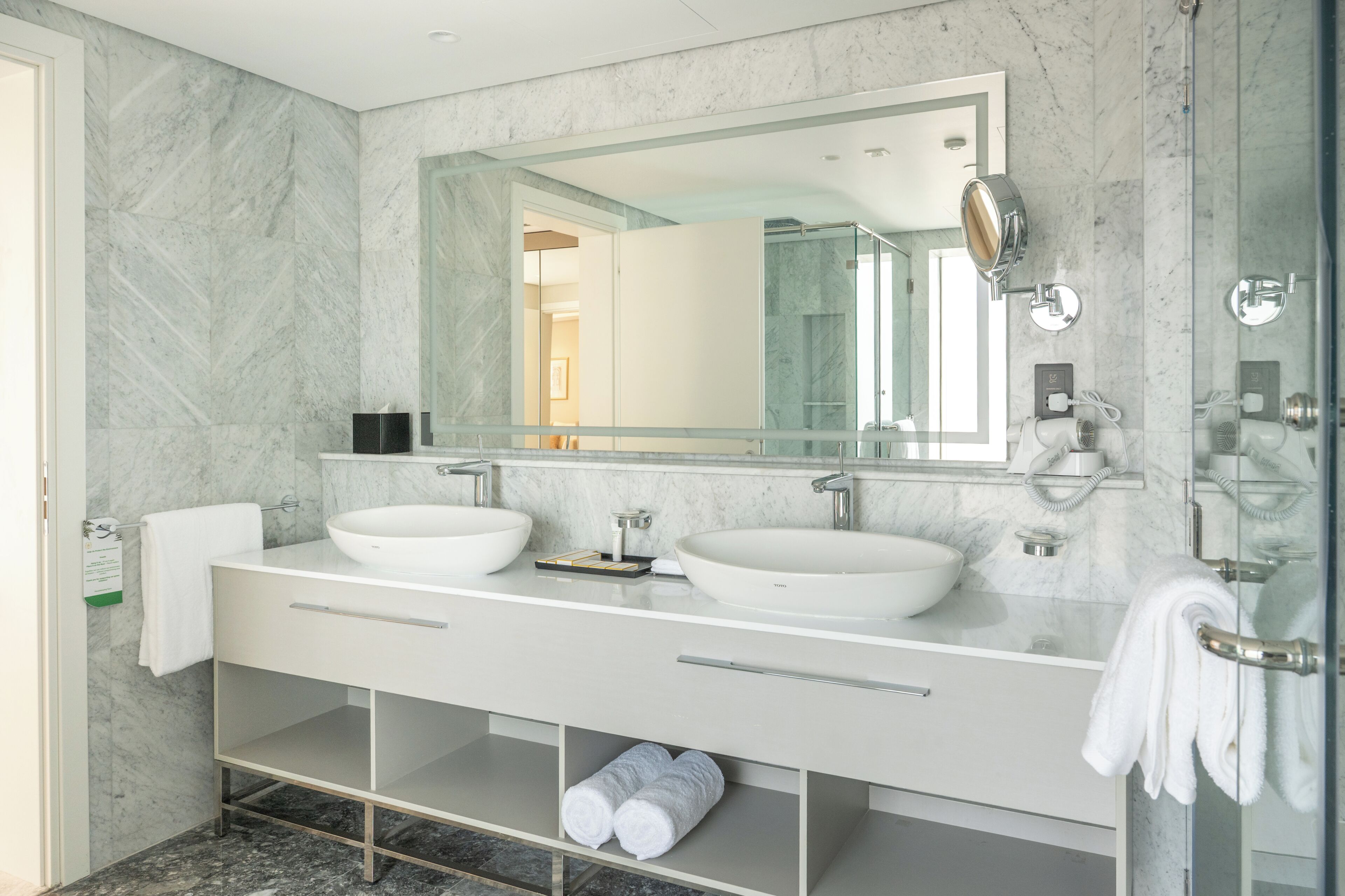 Un baño moderno con dos lavamanos, un espejo grande y una cabina de ducha con paredes de vidrio.