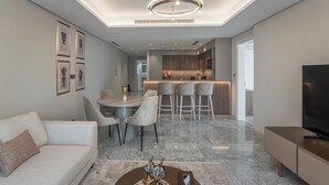 A modern living room with a sofa, dining table, and chairs, a kitchen area with a bar, and a flat-screen TV.