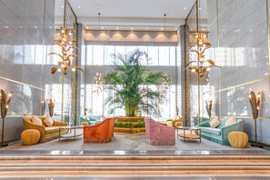 Un vestíbulo espacioso con una palmera grande, asientos modernos y un techo alto con iluminación decorativa.