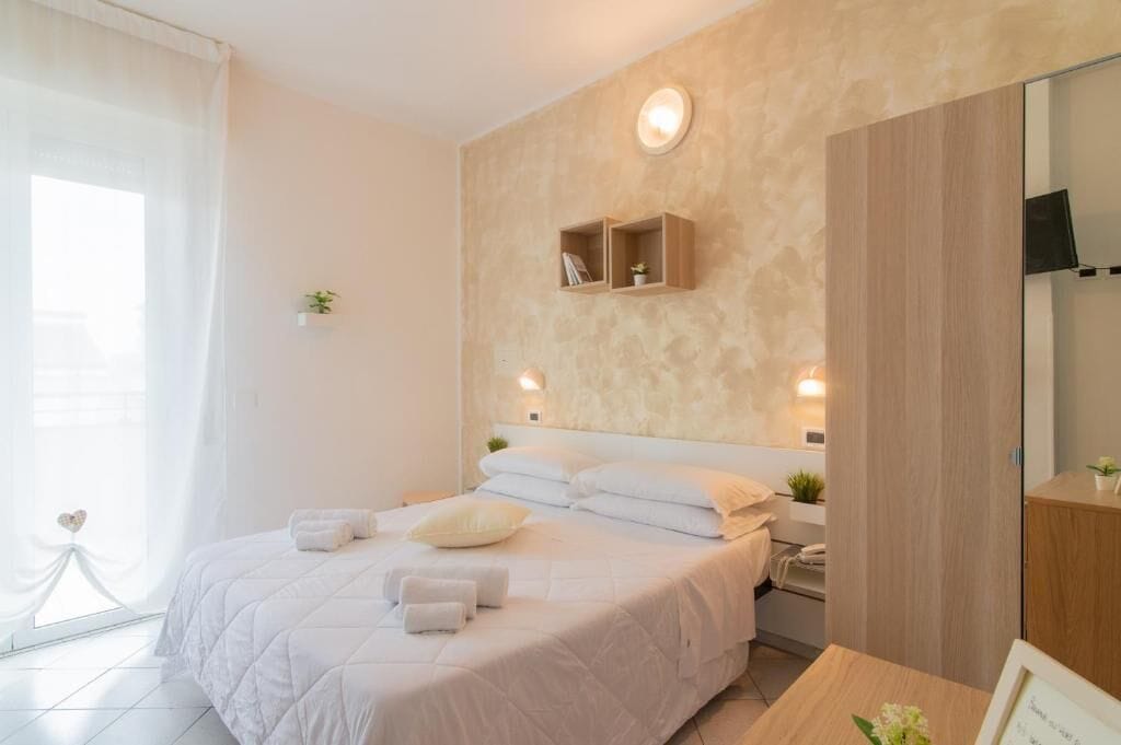 A modern bedroom with a large bed, bedside tables, a mirror, and a wall-mounted shelf.