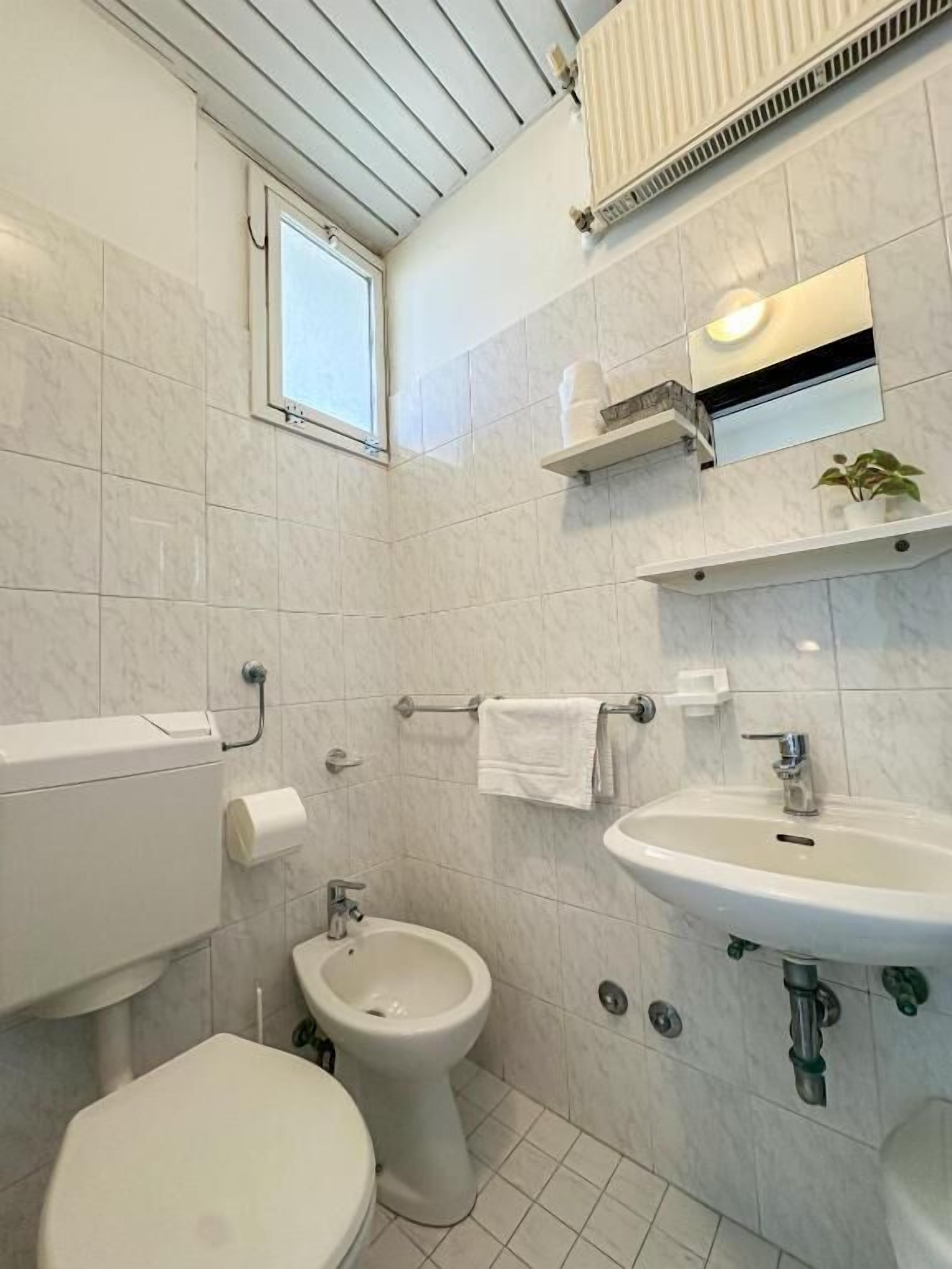 A bathroom with a toilet, bidet, sink, and a window.