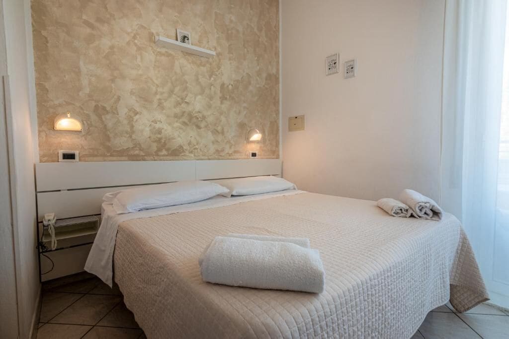 A neatly made bed with a quilted cover, a bedside telephone, and a wall-mounted shelf with a light fixture.