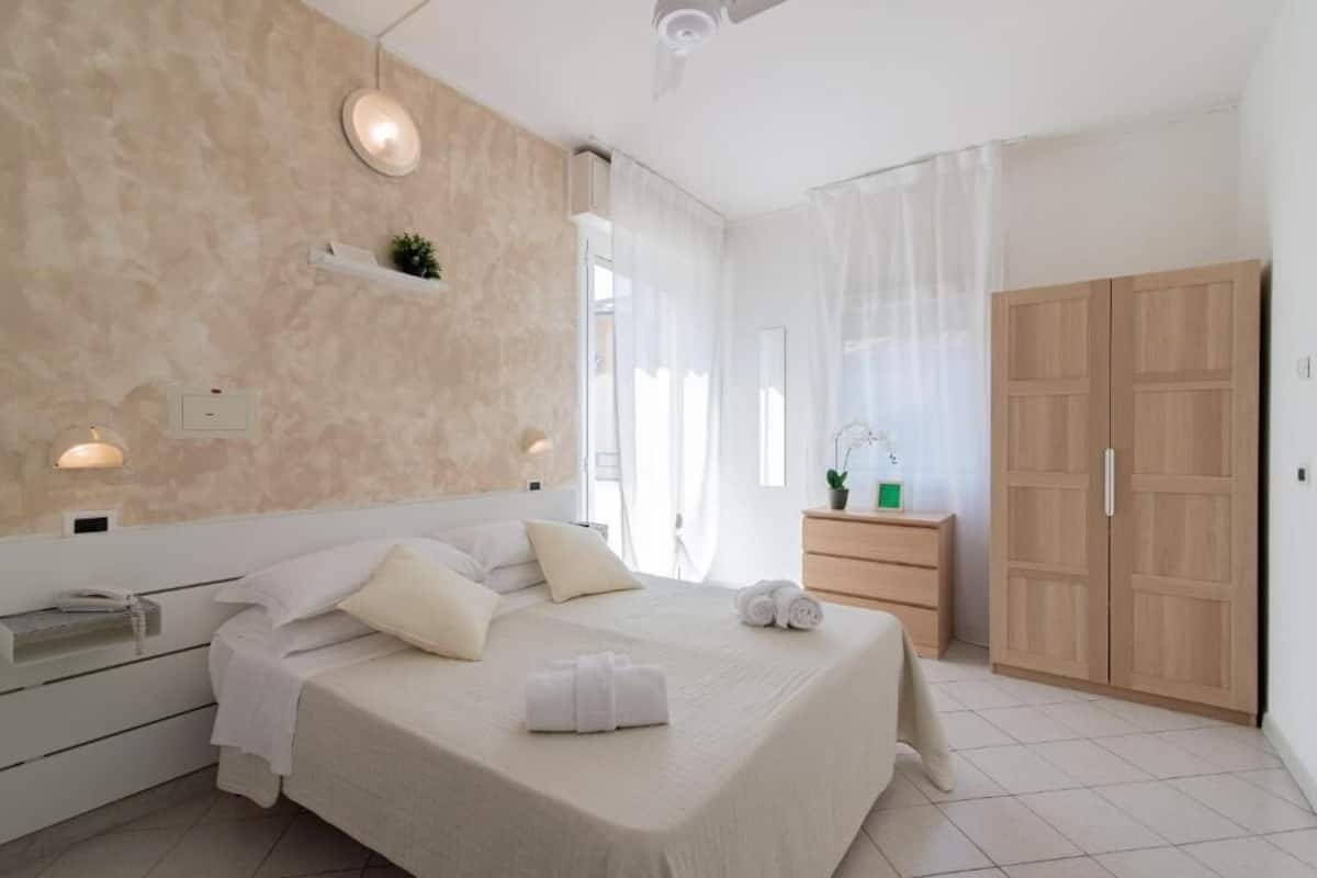 Un dormitorio con cama, mesita de noche, lámpara, armario y ventana con cortinas.