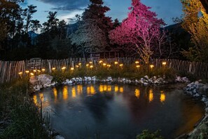 A pond with a wooden fence and lights, surrounded by trees and rocks. - WOODMOOD log cabin with wellness (Leuk)