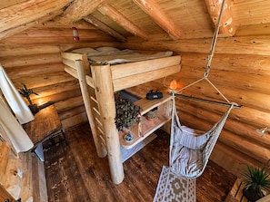 A wooden cabin interior with a bunk bed, a hanging chair, and a small shelf with plants and a speaker. - WOODMOOD log cabin with wellness (Leuk)