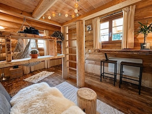 A cozy cabin interior with a wooden floor, a sofa, a dining area, and a window with curtains. - WOODMOOD log cabin with wellness (Leuk)