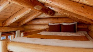 Dormitorio de cabaña de madera con cama, almohadas y ventana.