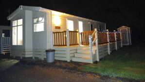 A single-story house with a porch, a small deck, and a visible trash can. - Beautiful 2 bed Caravan With Views of Dartmoor (Launceston)