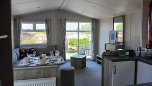 A cozy living room with a sofa, dining table set, and a kitchen area with cabinets and a countertop. - Beautiful 2 bed Caravan With Views of Dartmoor (Launceston)