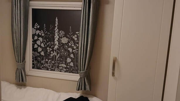 A bedroom with a bed, a window with curtains, and a door. - Beautiful 2 bed Caravan With Views of Dartmoor (Launceston)