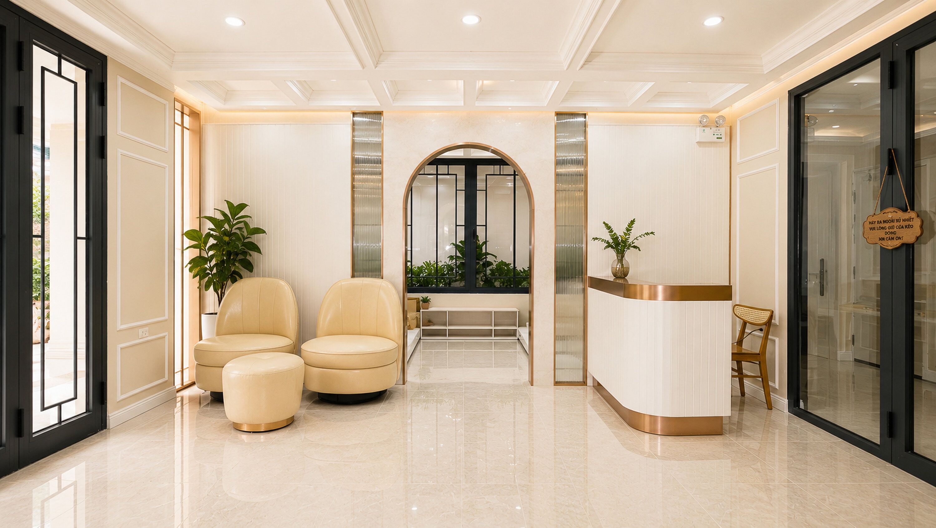 Zona de recepción con un mostrador curvo, dos sillones de cuero, una planta en maceta y una puerta de vidrio que da a otra habitación.