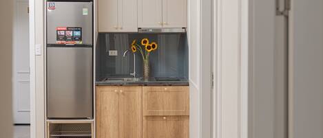 A compact kitchen with a refrigerator, wooden cabinets, a sink, and a vase with sunflowers.