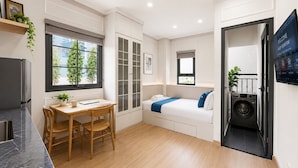 Habitación de hotel compacta con zona de comedor, cama con detalles azules, lavadora y una televisión mostrando un mensaje de bienvenida.