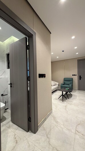 A modern hotel room with a marble floor, a green sofa, a small table, and a door leading to a bathroom. - 203 Tara-jre Jabal Al Lweibdeh With Stunning View (Amman)
