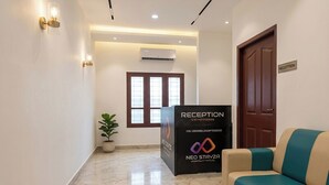 A reception area with a reception desk, a reception sign, a potted plant, and a sofa.