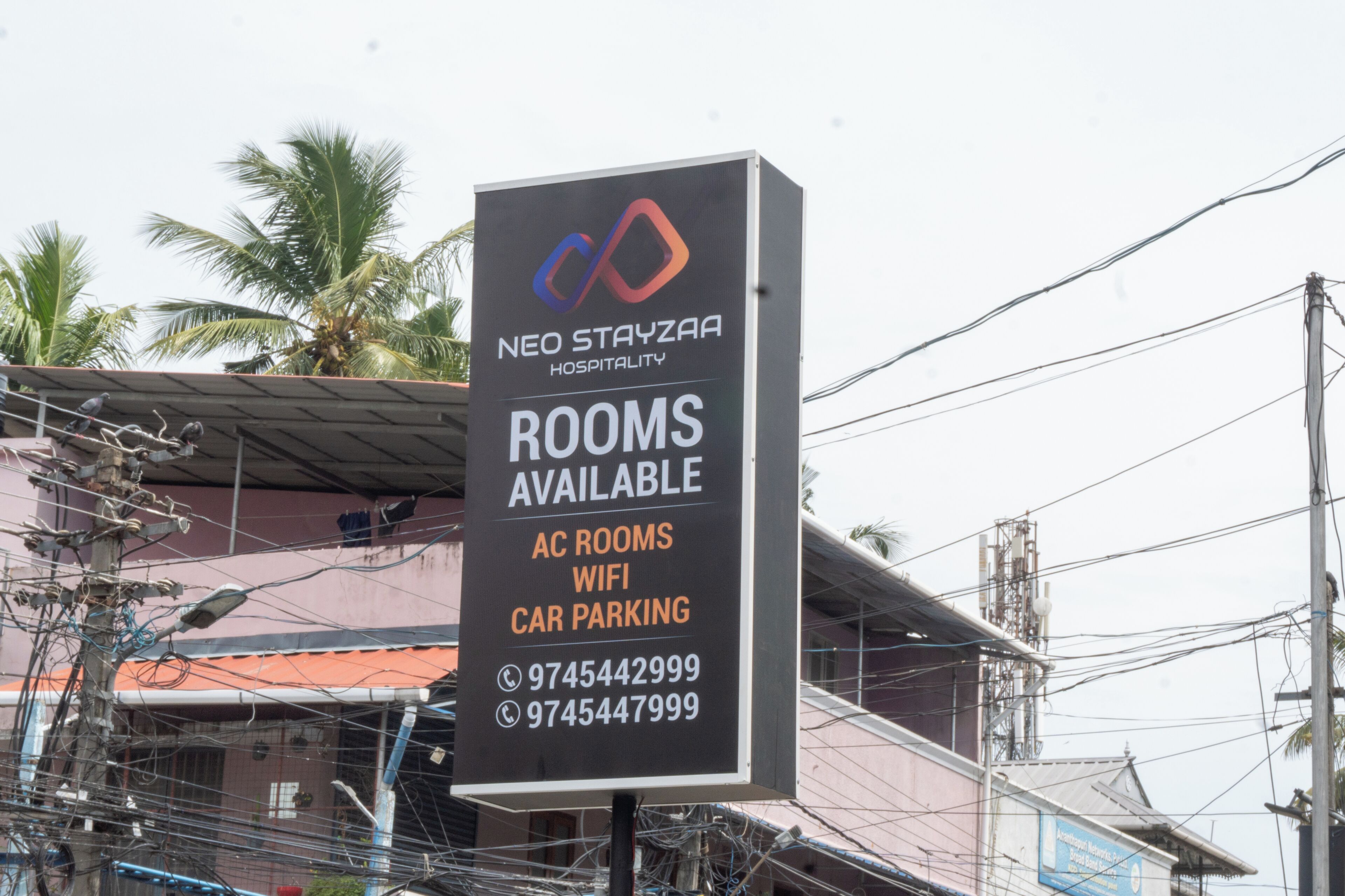 Letrero para NEO STAYZAA HOSPITALITY con comodidades como habitaciones con aire acondicionado, WIFI y estacionamiento para coches.