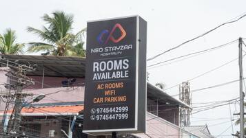 Letrero para NEO STAYZAA HOSPITALITY con comodidades como habitaciones con aire acondicionado, WIFI y estacionamiento para coches.