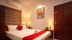 A hotel room with a bed, two bedside lamps, a door, and a wall-mounted air conditioner.