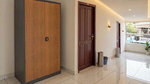 A hallway with a wooden wardrobe, a door, a trash bin, and a window with a view of a street.