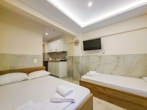 Une chambre d’hôtel avec un lit, un petit bureau, un téléviseur fixé au mur et, au fond, une kitchenette.