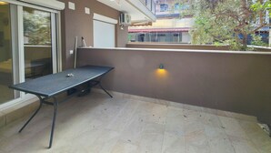 Ein Balkon mit einem Metalltisch, einer Schiebetür und einer Wandleuchte.