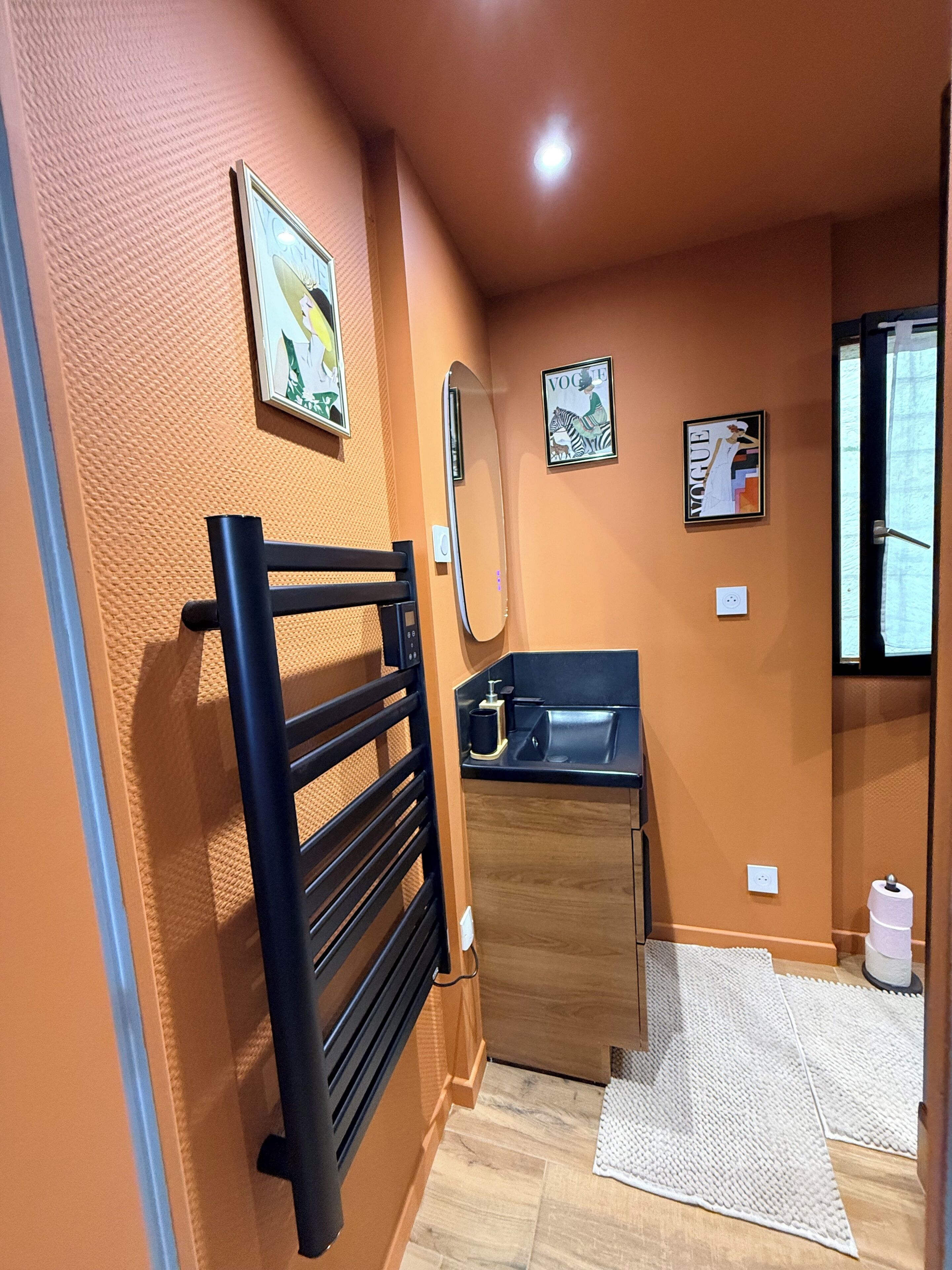 Un baño con toallero negro, espejo, lavabo e inodoro.