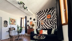 A living room with a zebra-patterned wall, a round coffee table, a sofa, a dining area with chairs, and a vintage radio. - The Zebra Club (Saumur)