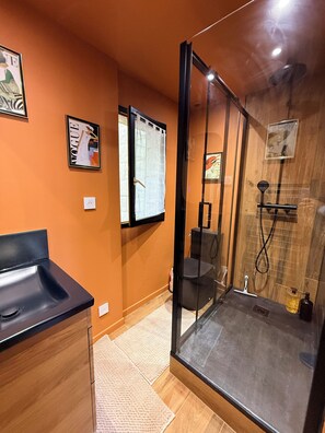 Une salle de bain moderne avec une douche à l’italienne en verre, un lavabo noir et un meuble-lavabo en bois.