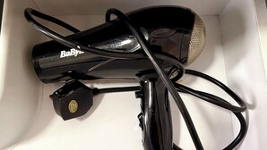 Ein schwarzer Haartrockner mit Kabel und Netzteil in einer weißen Schachtel.