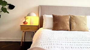 Ein ordentlich eingerichtetes Schlafzimmer mit Bett, Nachttisch, Lampe und Wandbildern.
