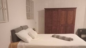 A bedroom with a bed, a wooden nightstand, a wardrobe, and a radiator. - Room-jasmin Cottage Brixton (Johannesburg)