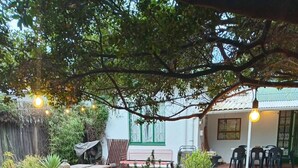 A patio area with wooden tables and benches, surrounded by potted plants and a brick pathway. - Room-jasmin Cottage Brixton (Johannesburg)