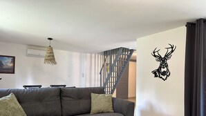Una sala moderna con un sofá gris, una mesa de centro de madera, una escalera y un adhesivo mural con forma de ciervo.