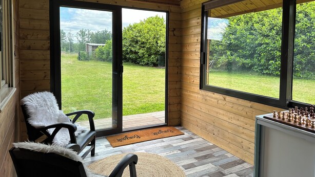 Una habitación con paneles de madera, una mesa de ajedrez, un sillón mullido y vistas a un patio césped a través de amplios ventanales.