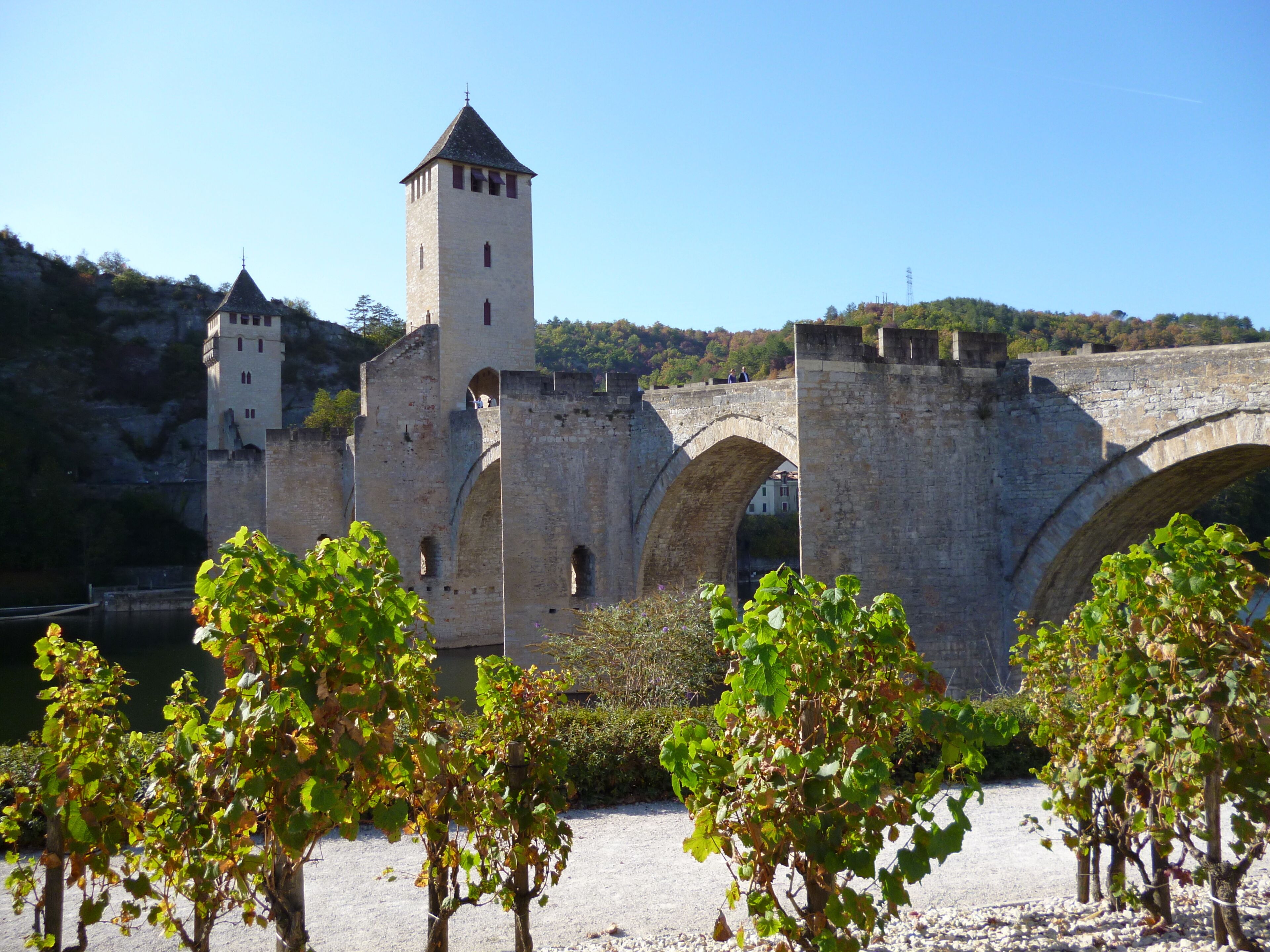 A historic stone bridge with arches, a tower, and a castle-like structure in the background.