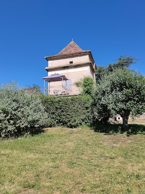 A building with a tiled roof, a balcony with a table and chairs, and a garden area in front.