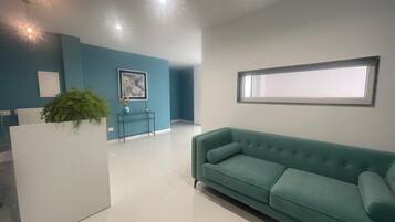 Un salon moderne avec un canapé de couleur turquoise, une console blanche et un tableau encadré accroché au mur.