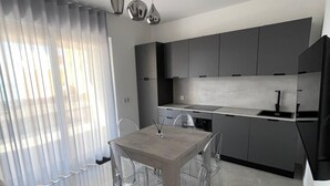 A modern kitchen with a dining area, featuring a large table and chairs, a built-in oven, and a pendant light. - Gheloi Apartments (Gela)