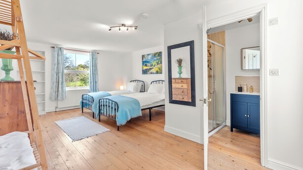 Quarto com cama, escada de madeira, janela com cortinas, um quadro e banheiro com armário azul.
