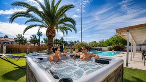 A hot tub with two people, a pool, and a hammock in a backyard. - 7BR Vegas Oasis • Big Pool • Games • Near Strip (Las Vegas)
