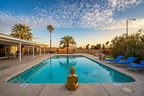 Ein Swimmingpool mit Buddha-Statue, Liegestühlen und Palmen.