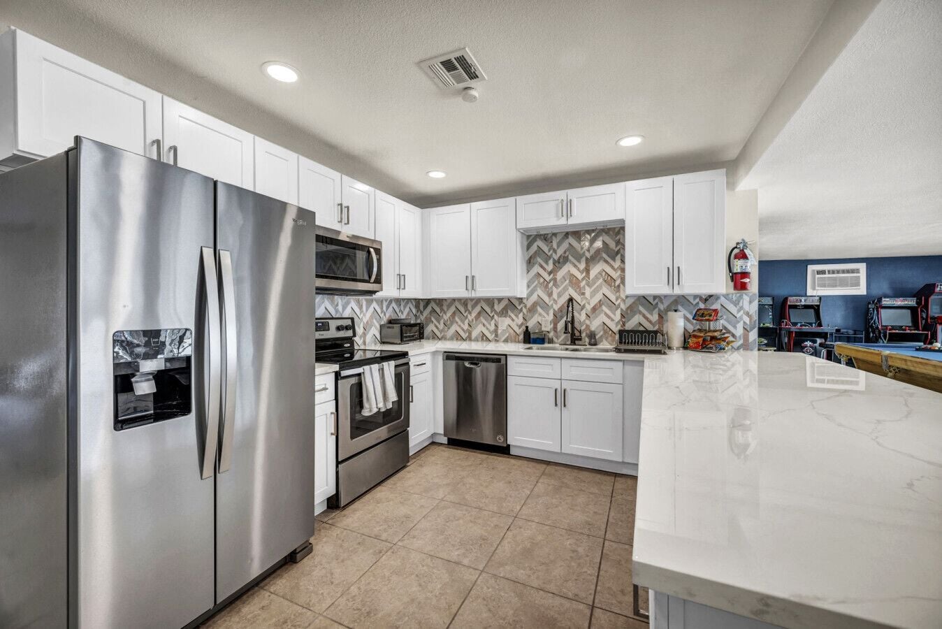 A modern kitchen with stainless steel appliances, white cabinets, a herringbone tile backsplash, and a marble countertop.
