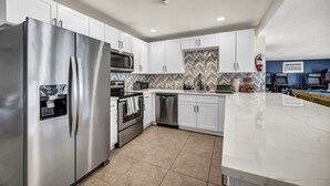 A modern kitchen with stainless steel appliances, white cabinets, a herringbone tile backsplash, and a marble countertop. - 7BR Vegas Oasis • Big Pool • Games • Near Strip (Las Vegas)