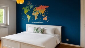Camera da letto con un letto bianco, una mappa del mondo appesa al muro e un tappeto blu con la scritta 'UNDER THE' visibile.