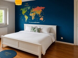 Ein Schlafzimmer mit einem weißen Bett, einer Weltkarte an der Wand und einem blauen Teppich, auf dem 'UNDER THE' zu sehen ist.