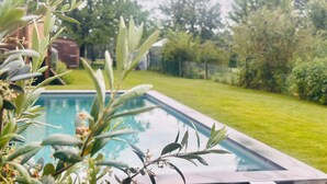 Una piscina circondata da vegetazione e un edificio in mattoni sullo sfondo.