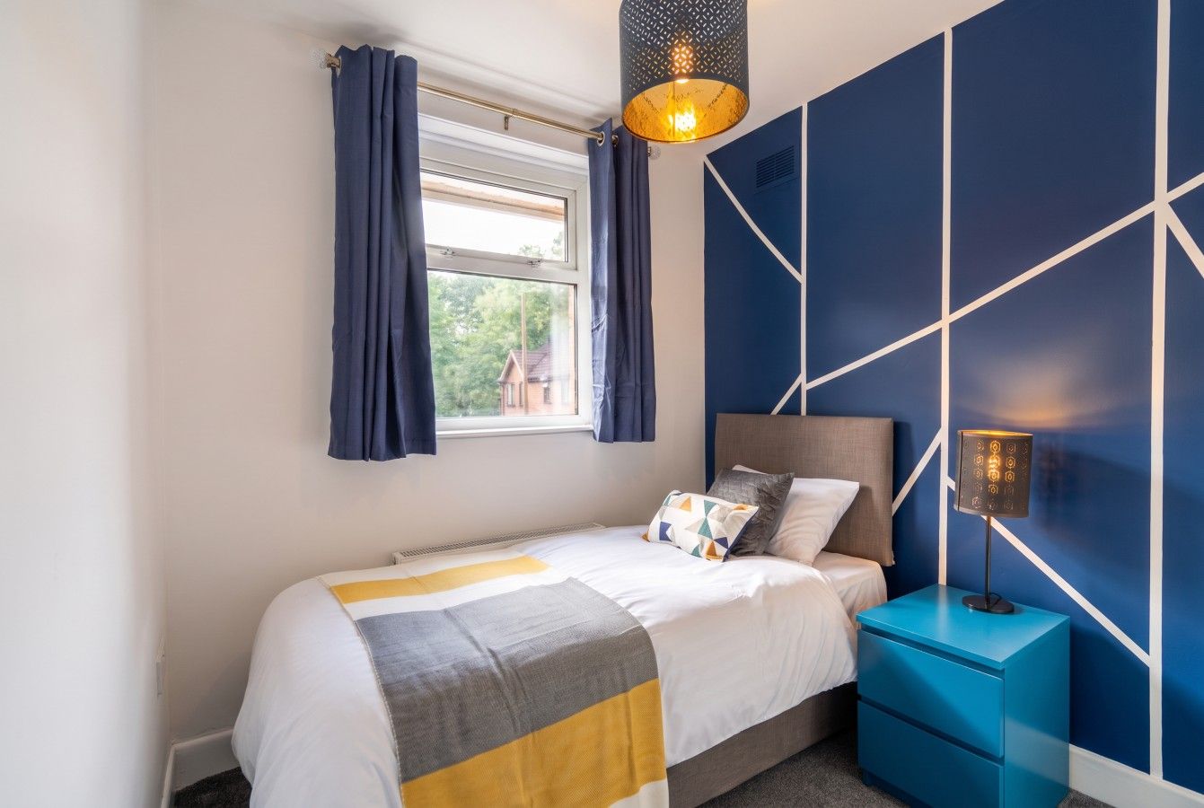 A bedroom with a bed, a nightstand, a lamp, and a window with curtains.