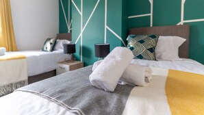 Ein Hotelzimmer mit zwei Betten, jedes mit unterschiedlicher Bettwäsche, einem Nachttisch mit Lampe und einer Wand mit geometrischem Muster.